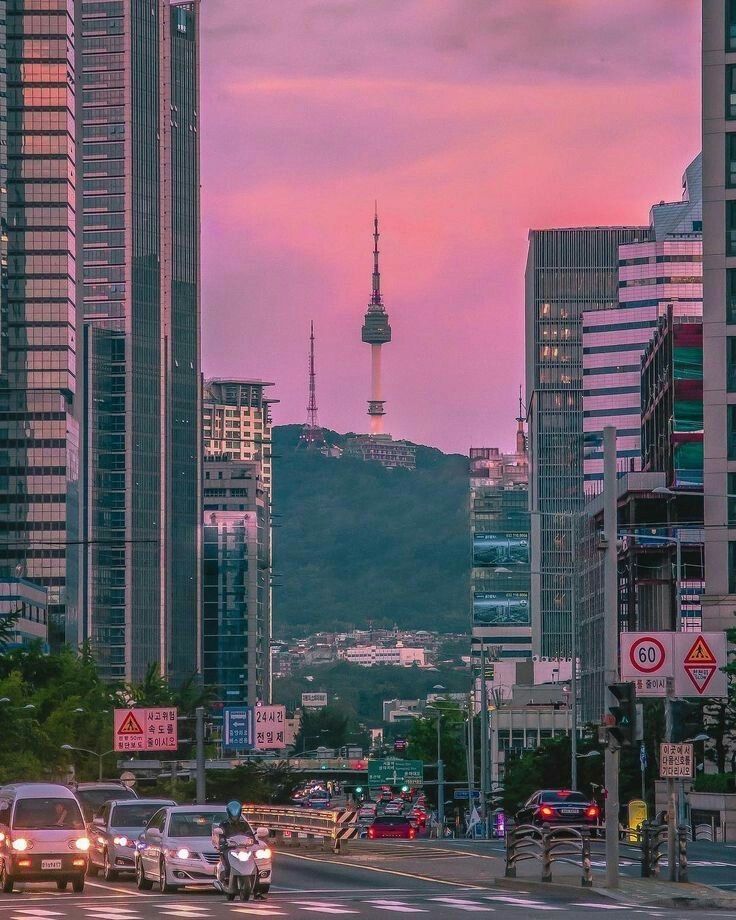 cars are driving down the street in front of tall buildings with a tv tower in the background