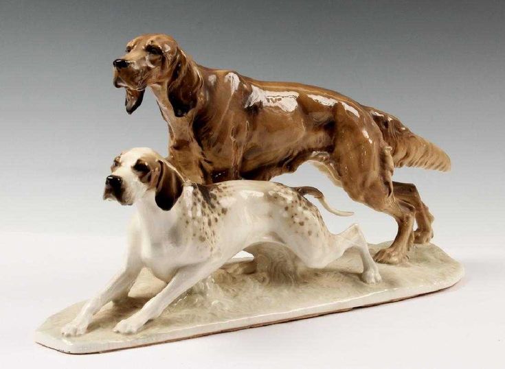 two figurines of dogs standing on top of a white base with brown spots