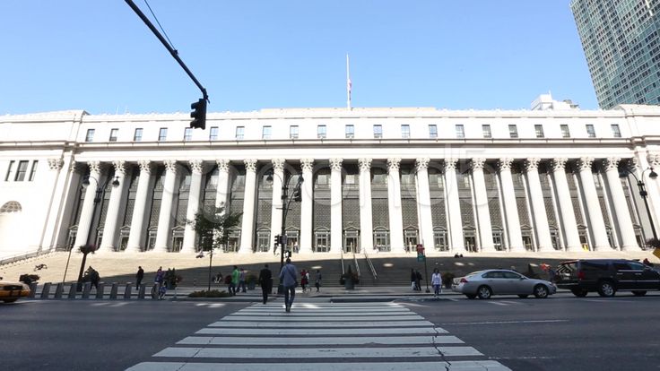 people are crossing the street in front of a large white building with columns and pillars