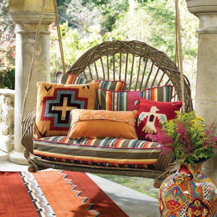 a hanging chair with colorful pillows on it and a vase full of flowers next to it