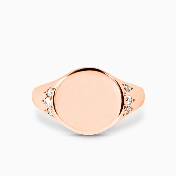 a rose gold signet ring with three diamonds on the front and center, set against a white background