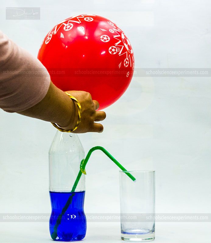 a person holding a red balloon in a vase with blue liquid and a green straw