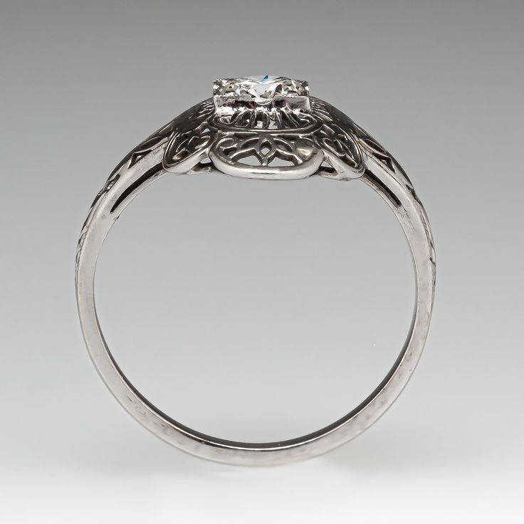 This lovely circa 1930s ring features an 18K white gold gallery and is finished with a 14K white gold shank. The ring features a pierced and engraved design with milgrain details and is centered with one (1) round transitional brilliant cut diamond. The ring measures 18.4mm at the top, rises 4.3mm above the finger, tapering to 1.6mm wide and 1.2mm thick at the base of the shank. This ring is currently a size 6. The ring shows gentle overall wear. Vintage Engraved Ring With Single Diamond For Formal Occasions, Vintage Sterling Silver Diamond Ring For Formal Occasions, Formal 14k White Gold Filigree Ring, Vintage White Gold Engraved Diamond-cut Ring, Vintage White Gold Diamond Cut Engraved Ring, Vintage White Gold Engraved Ring With Diamond Cut, Antique White Gold Ring With Single Diamond, Antique Solitaire Diamond Ring For Formal Occasions, Vintage White Gold Diamond Ring With Single Diamond