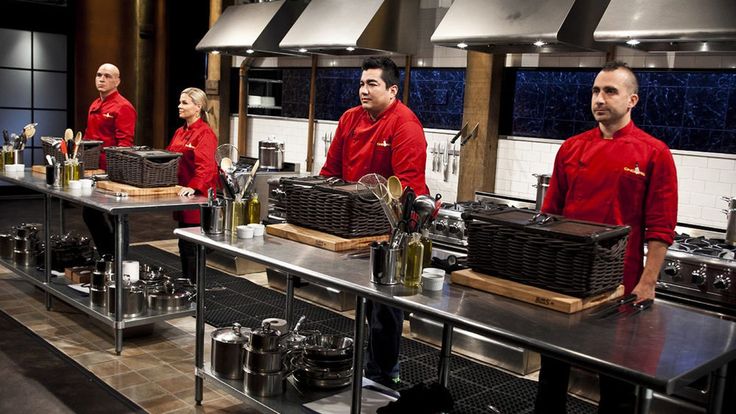 three men in red shirts are standing at the kitchen counter with baskets and bottles on it