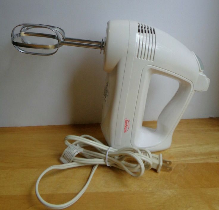 a white electric hand mixer sitting on top of a wooden table next to a wall