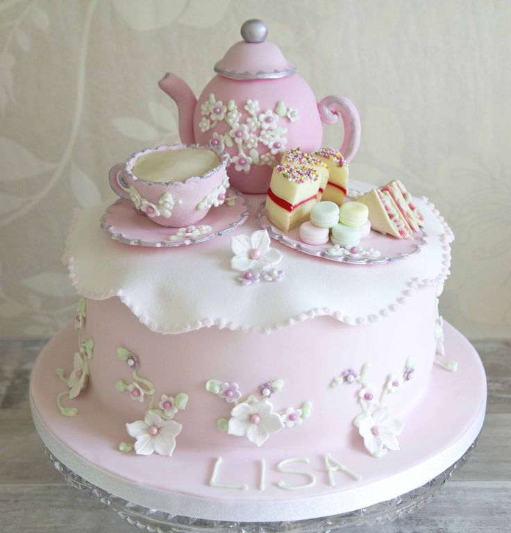 a pink cake with white frosting and flowers on it, topped with a teapot