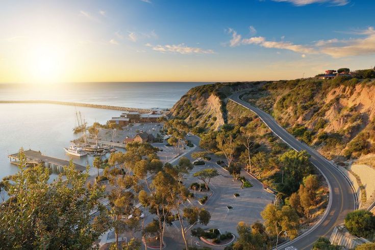 an aerial view of a road and the ocean at sunset, with boats in the water