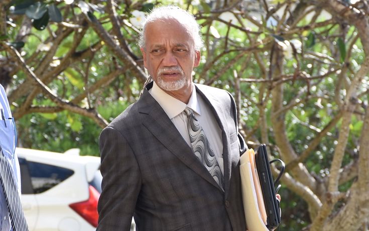 an older man in a suit and tie holding a hot dog while walking towards the camera