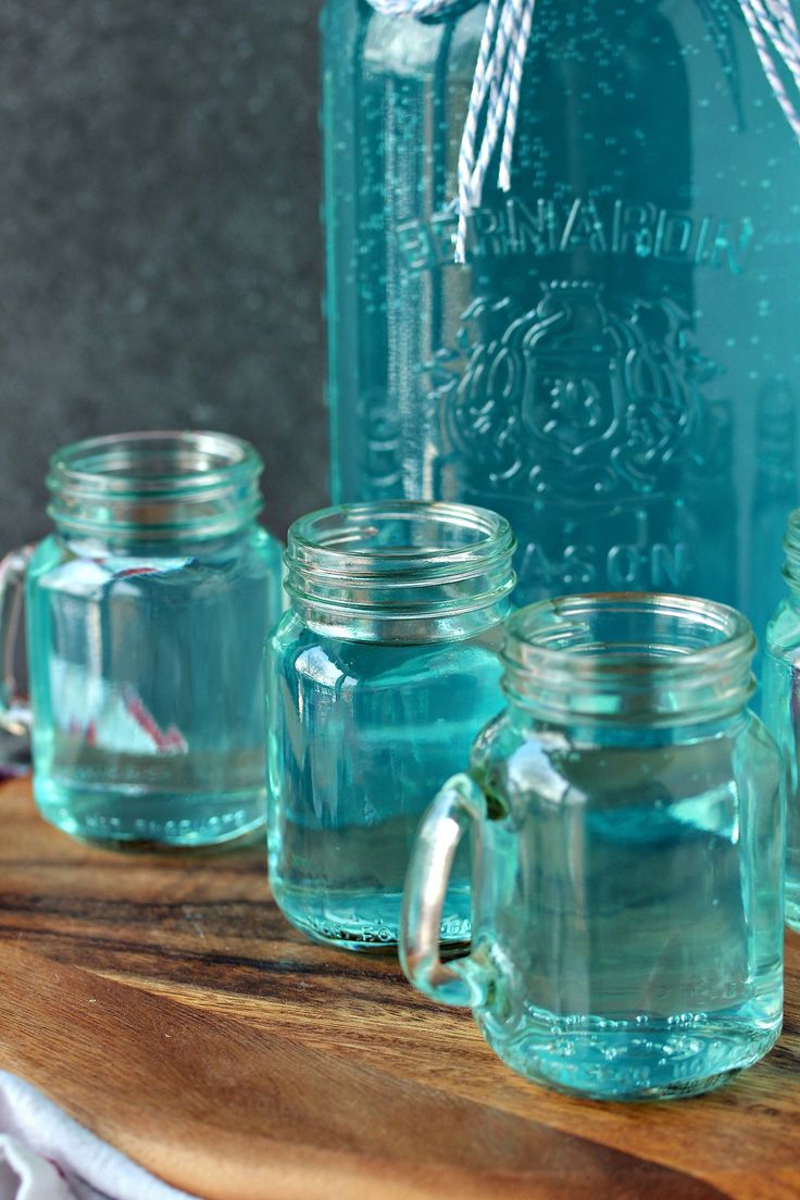 four mason jars are lined up on a wooden table next to a blue glass bottle