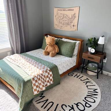 a teddy bear sitting on top of a bed in a room with gray walls and carpet