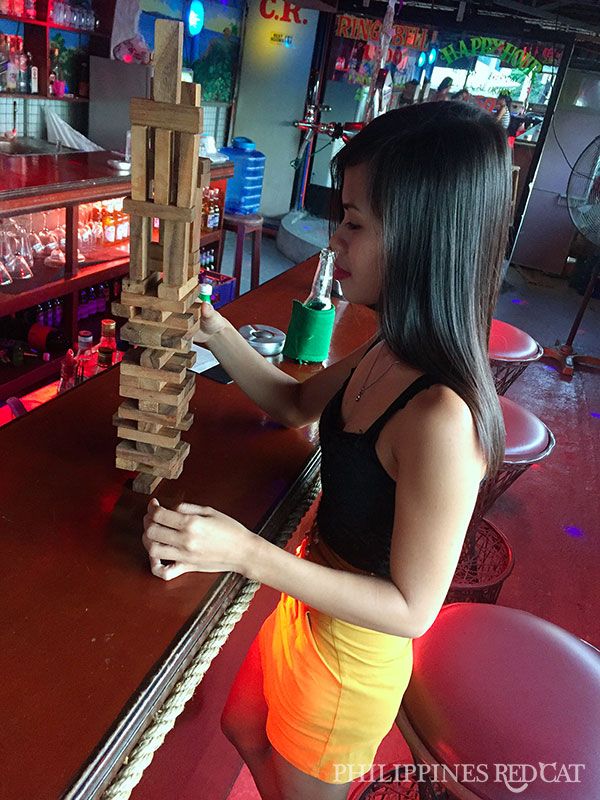 a woman standing in front of a wooden block tower on top of a table next to a bar