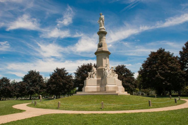 a monument in the middle of a grassy area with trees around it and a path leading up to it