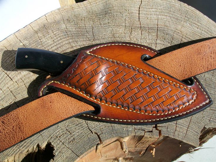 a leather knife holder on top of a tree stump with a black handle and brown stitching