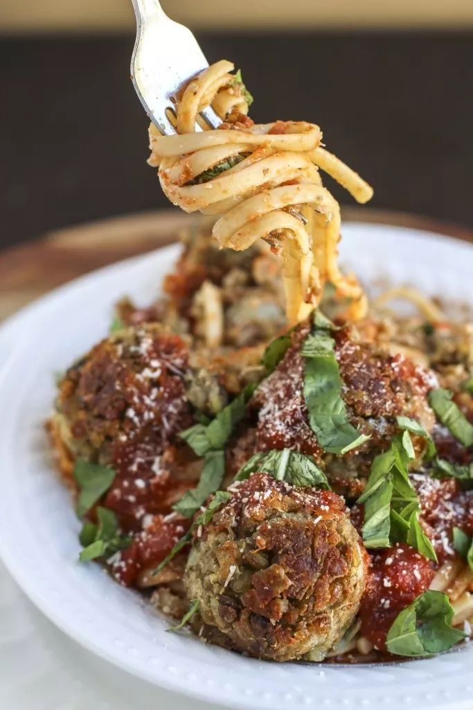 spaghetti and meatballs on a white plate with a fork sticking out of the top