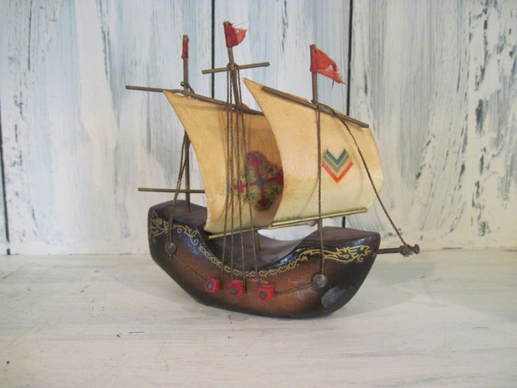 a wooden model ship with sails and flags on the front, sitting on a white surface