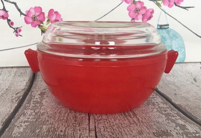 a large red bowl sitting on top of a wooden table next to a vase with pink flowers