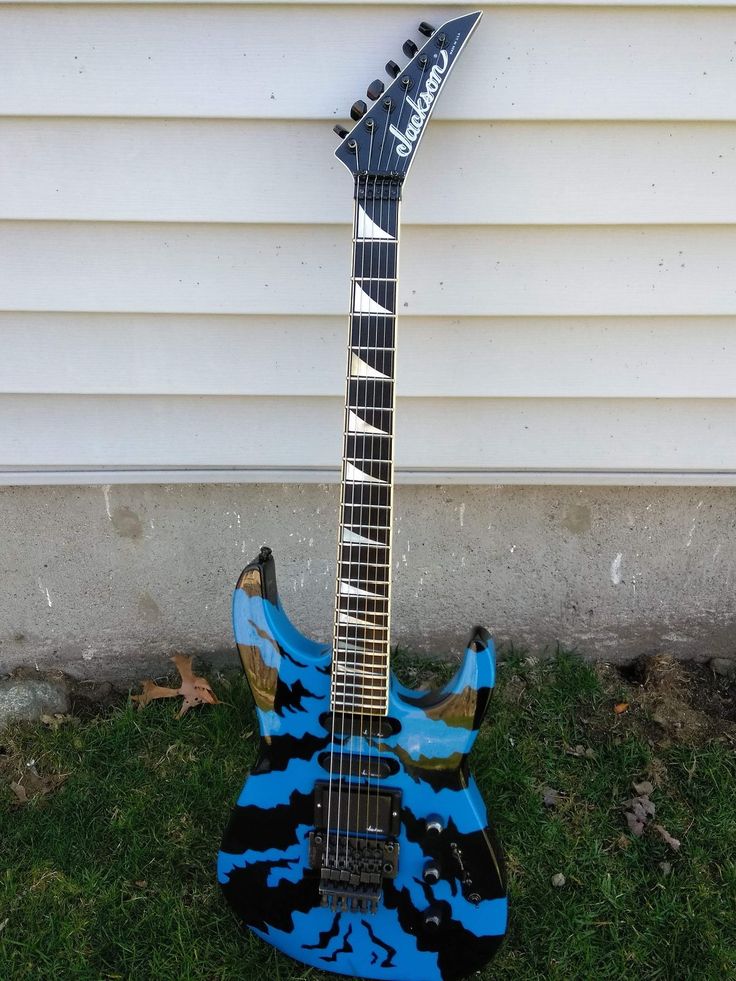 a blue and black guitar sitting on top of the grass next to a building with white siding