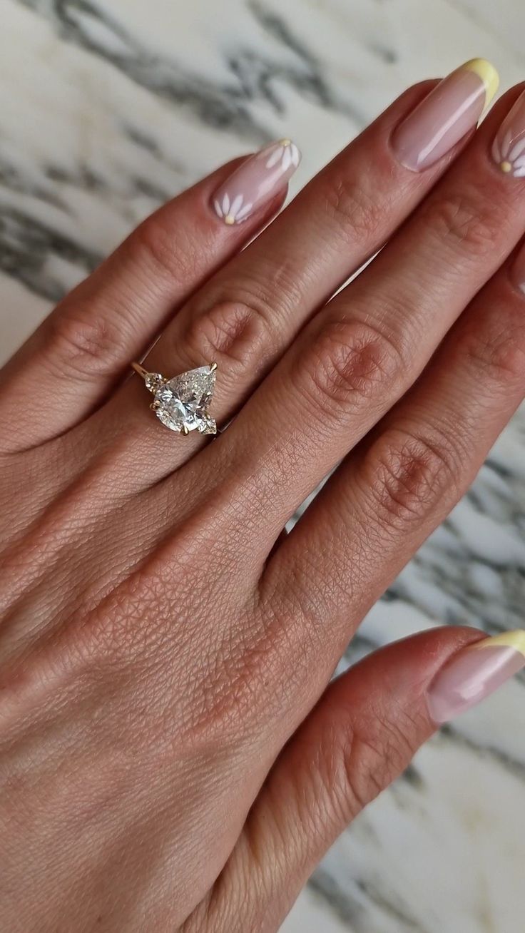 a woman's hand with pink and yellow manicured nails holding an engagement ring