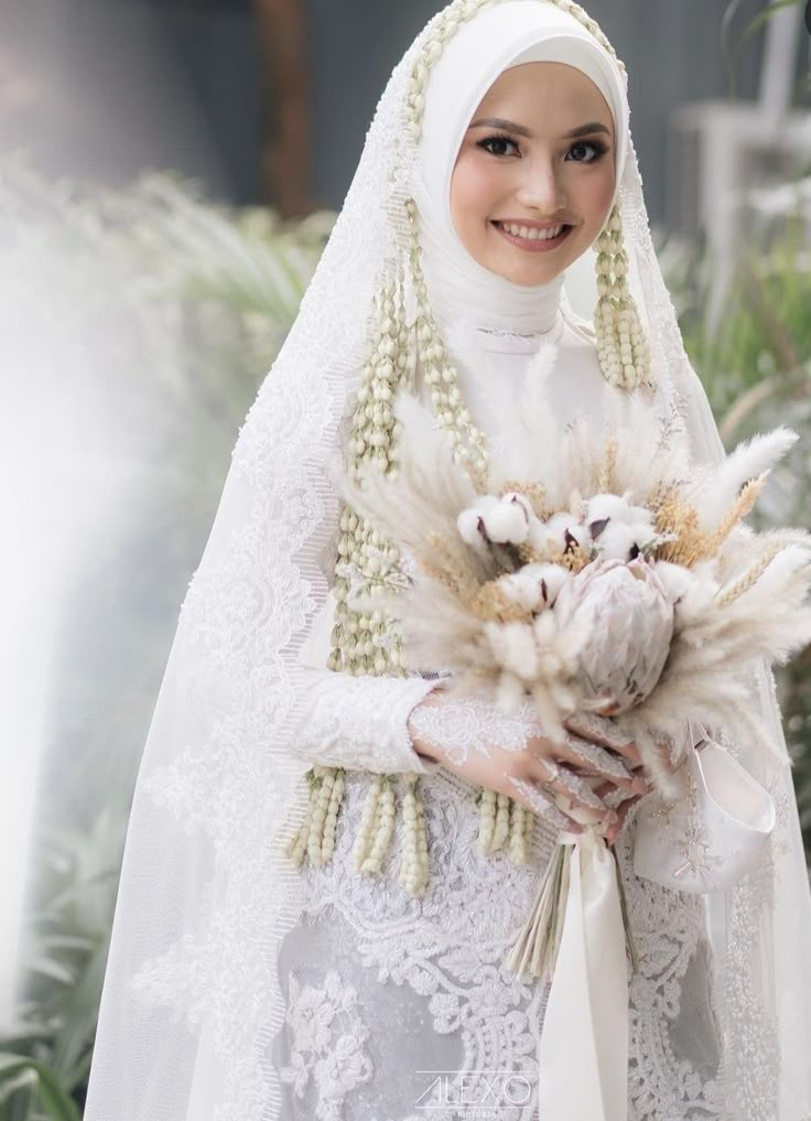 a woman in a white dress holding a bouquet of flowers and wearing a headscarf