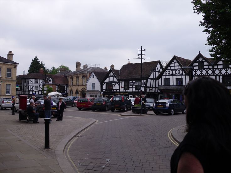 a woman standing on the side of a road next to parked cars and people walking around