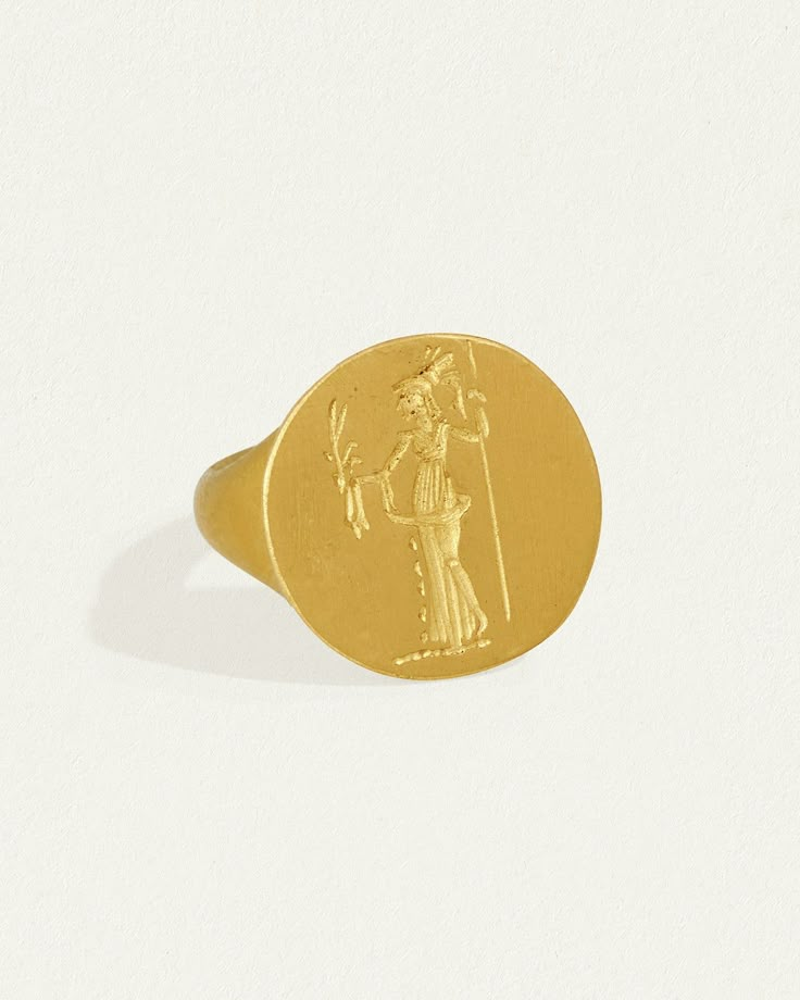 Made from 24k solid gold with a silky, satin finish, the  Heritage Ring Minerva has a rich, tactile lustre.   
  Featuring a hand-engraved depiction of Minerva - the ancient Roman equivalent of the Greek goddess Athena - clasping a spear and olive branch, symbolising protection and prosperity.   
  Each piece is carved by hand, ensuring that every ring is unique. Greek Goddess Athena, Ancient Artefacts, Greek Ring, Goddess Athena, Goddess Jewelry, Seal Ring, Athena Goddess, Gold Signet Ring, Olive Branch