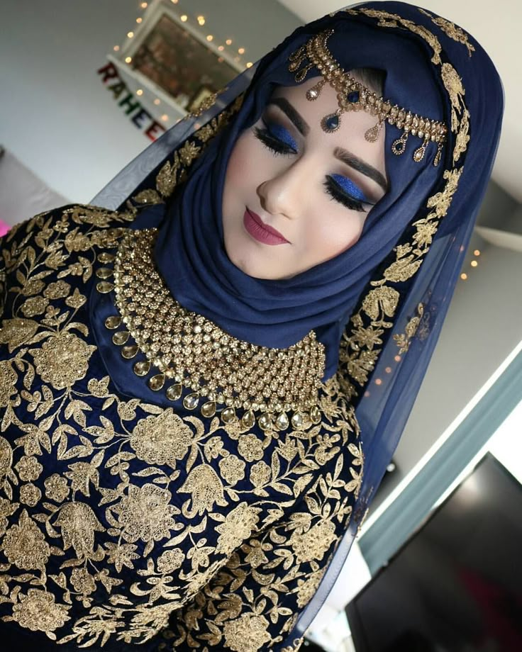 a woman in a blue and gold outfit with jewelry on her head is looking at the camera