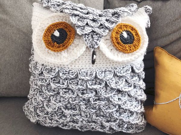 an owl pillow sitting on top of a gray couch next to a yellow throw pillow