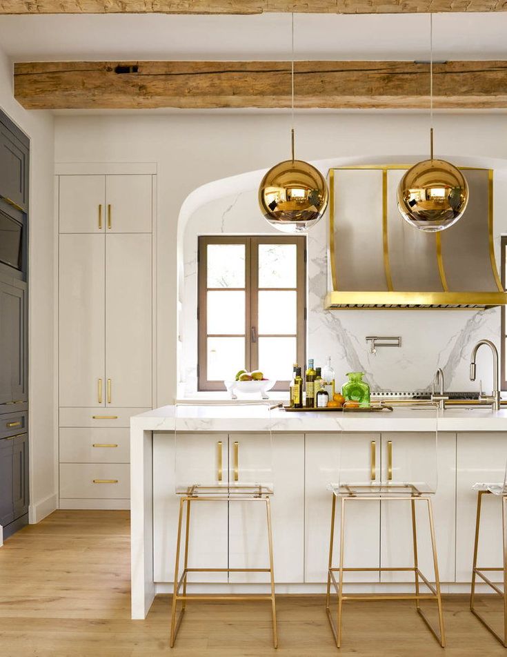 a kitchen with white counter tops and gold pendant lights hanging from the ceiling over the island