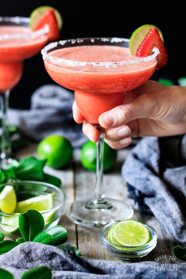 two margaritas in coupe glasses with lime slices on the rim and one being held by a hand