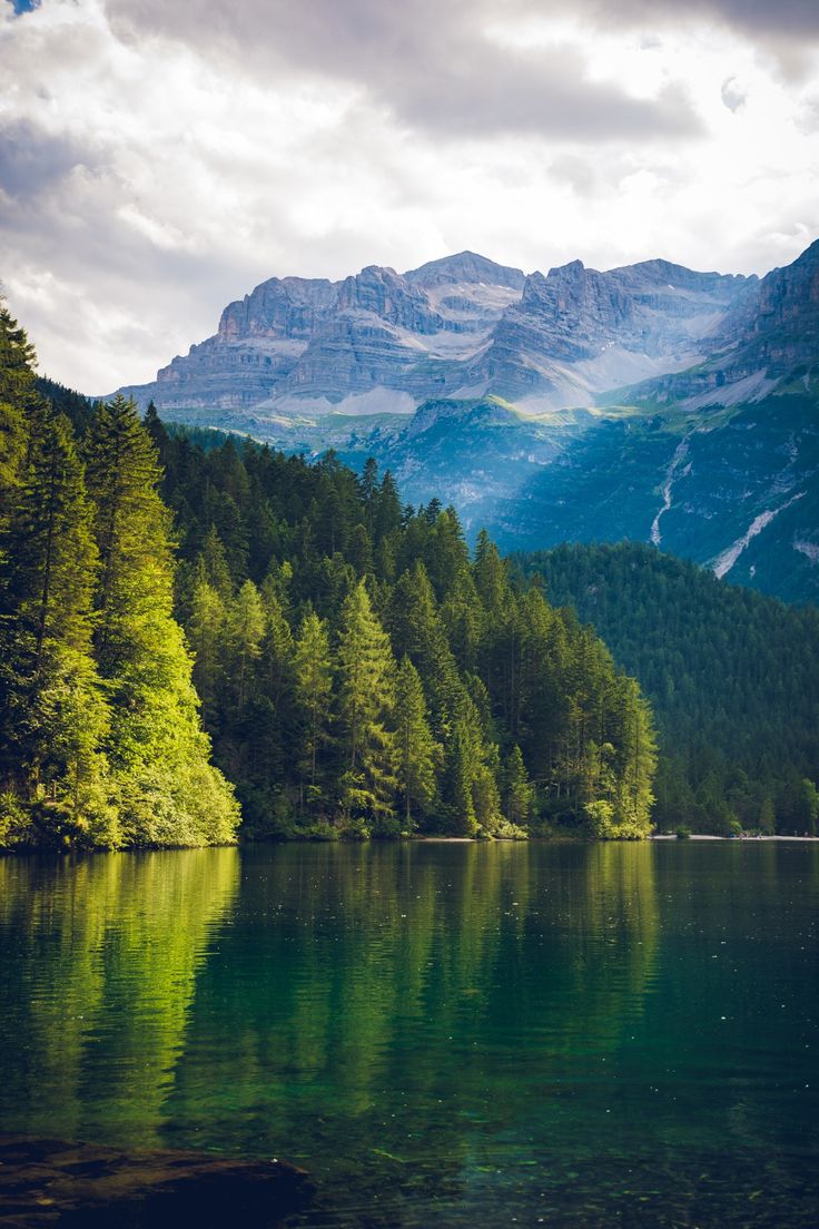 a lake surrounded by trees and mountains under a cloudy sky