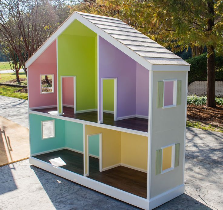 a multicolored doll house sitting on top of a cement ground next to trees