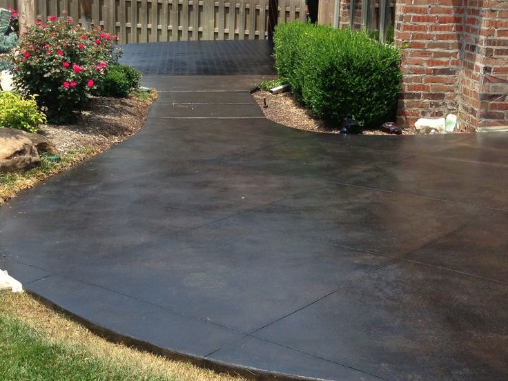 a black concrete walkway in front of a brick building with flowers and bushes on either side