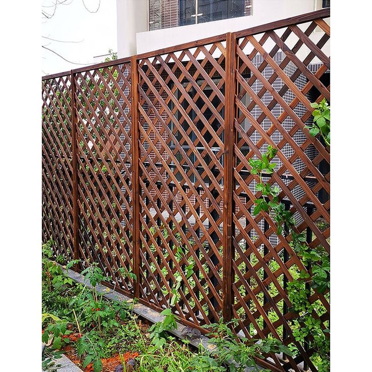 a wooden fence in front of a building with plants growing on the side and behind it