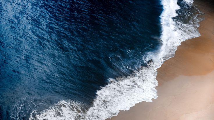 an aerial view of the ocean and beach from above, with waves crashing on the sand