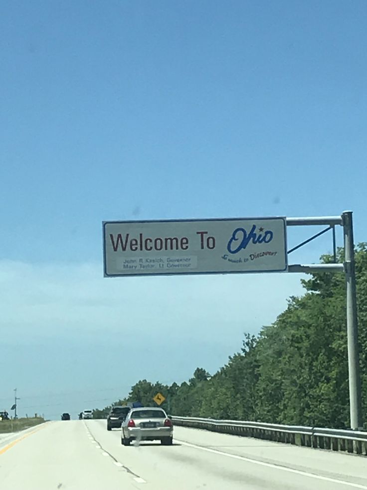 a welcome to ohio sign hanging from the side of a highway with trees in the background