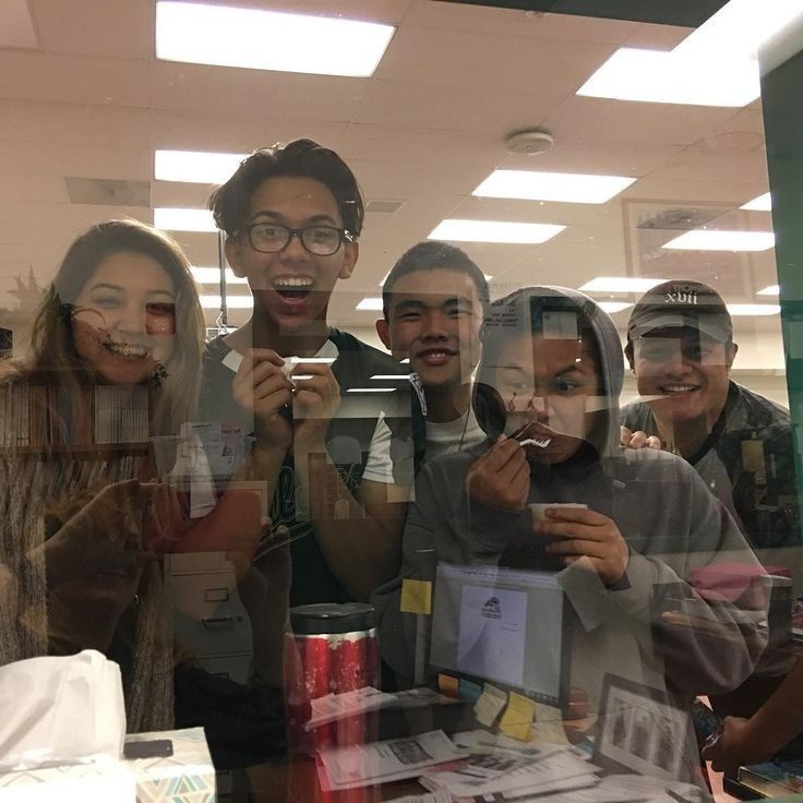 a group of people standing around each other in front of a glass window holding up their cell phones