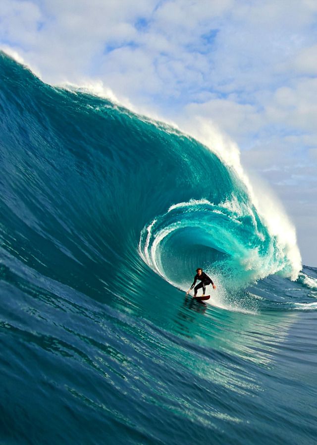 a man riding a wave on top of a surfboard in the ocean under a cloudy blue sky