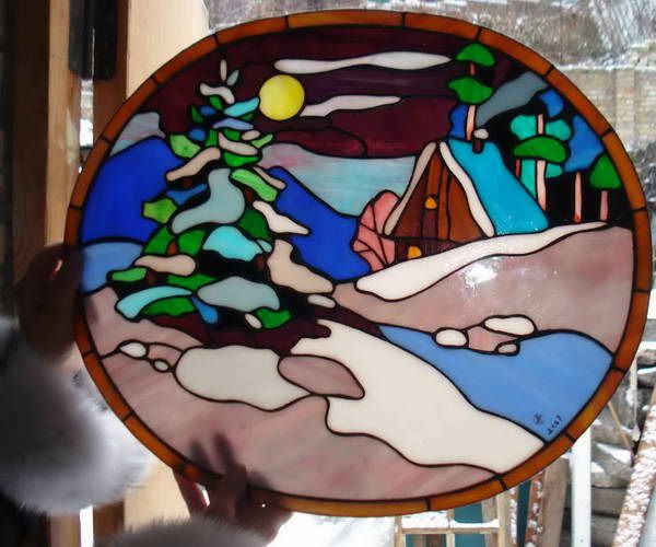 a hand holding up a stained glass window with a small house in the snow on it