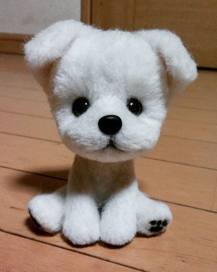 a small white stuffed dog sitting on top of a wooden floor next to a door