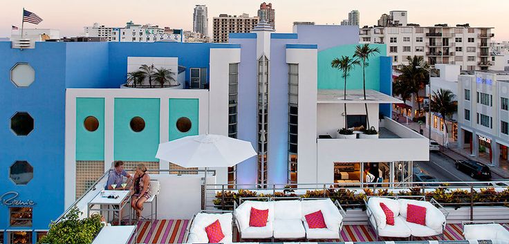 an outdoor lounge area with white and red pillows on top of the building, overlooking cityscape