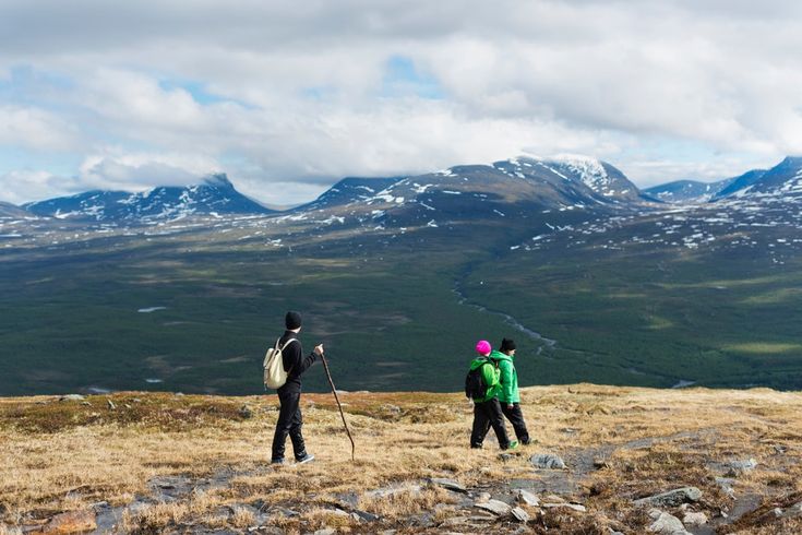 two people standing on top of a grass covered hill with mountains in the background,