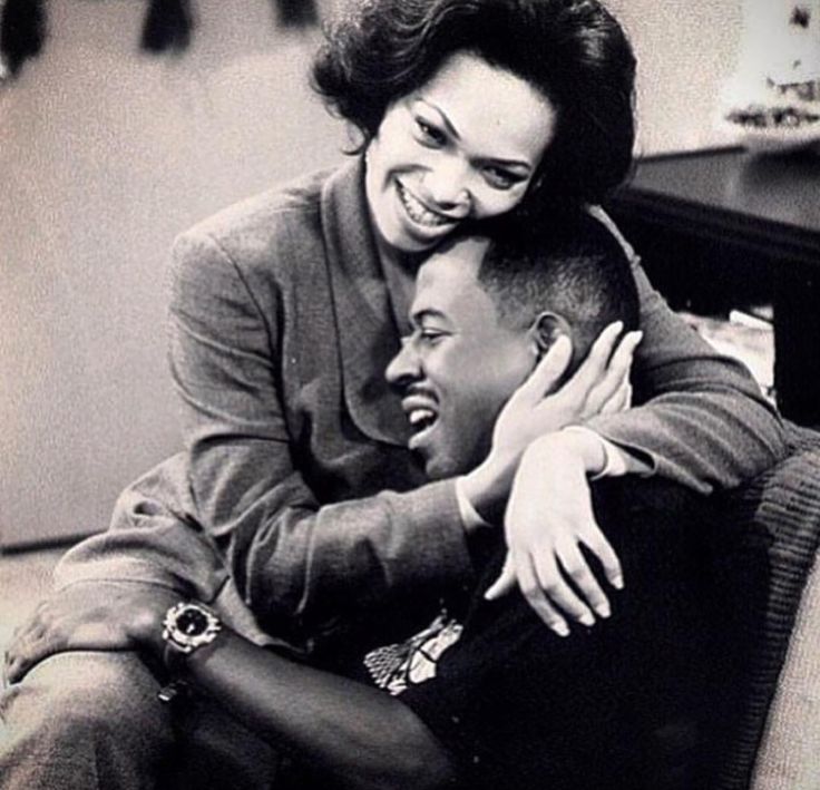 a woman hugging a man who is sitting on a couch