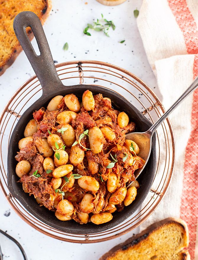 a skillet filled with beans and meat on top of a table next to bread