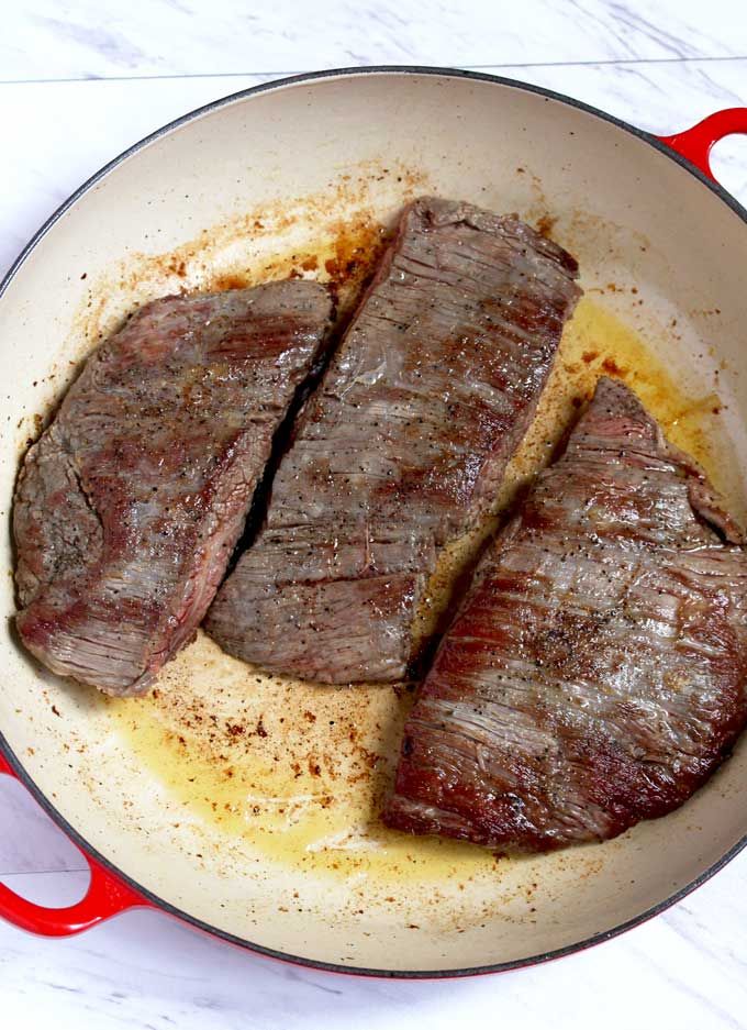 two steaks are cooking in a pan on the stove top, with yellow sauce