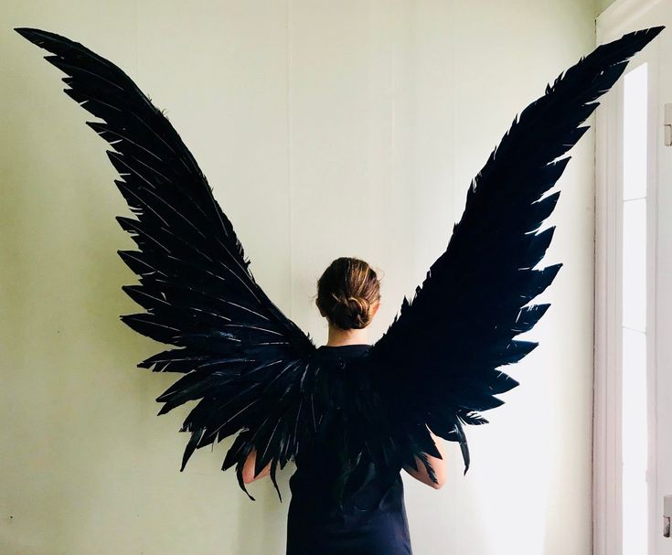 a woman standing in front of a wall with large black wings on it's back