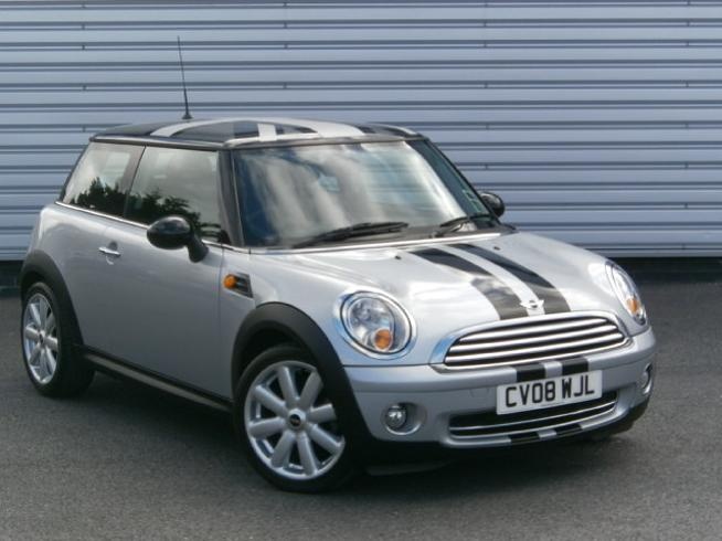 a silver mini car parked in front of a garage door next to a metal wall