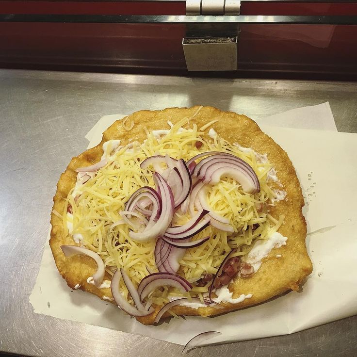 a pizza topped with onions and cheese on top of a metal counter next to a knife