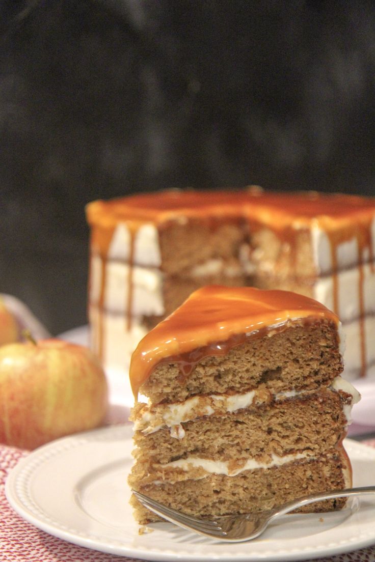 a slice of cake with caramel drizzled on top and an apple in the background