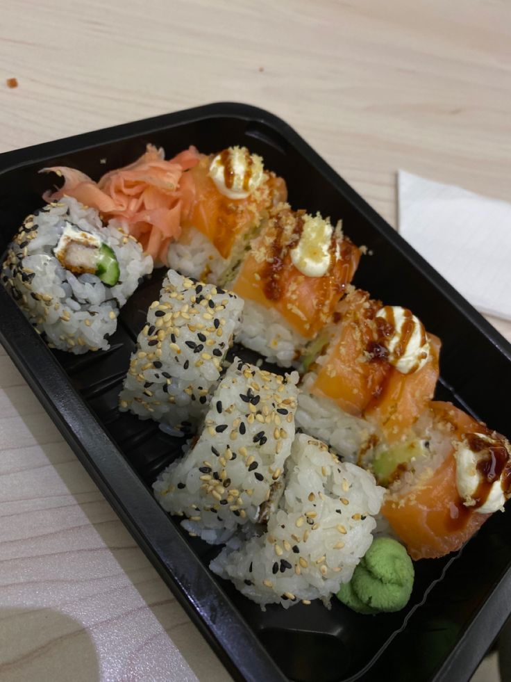 a black tray filled with sushi on top of a wooden table