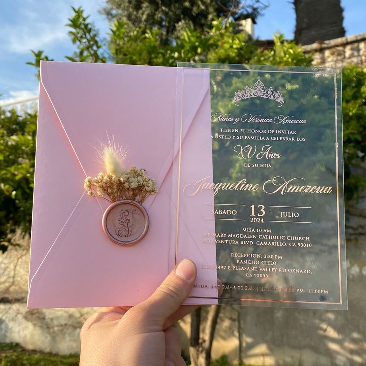 a person holding up a pink wedding card with a ring on it's finger